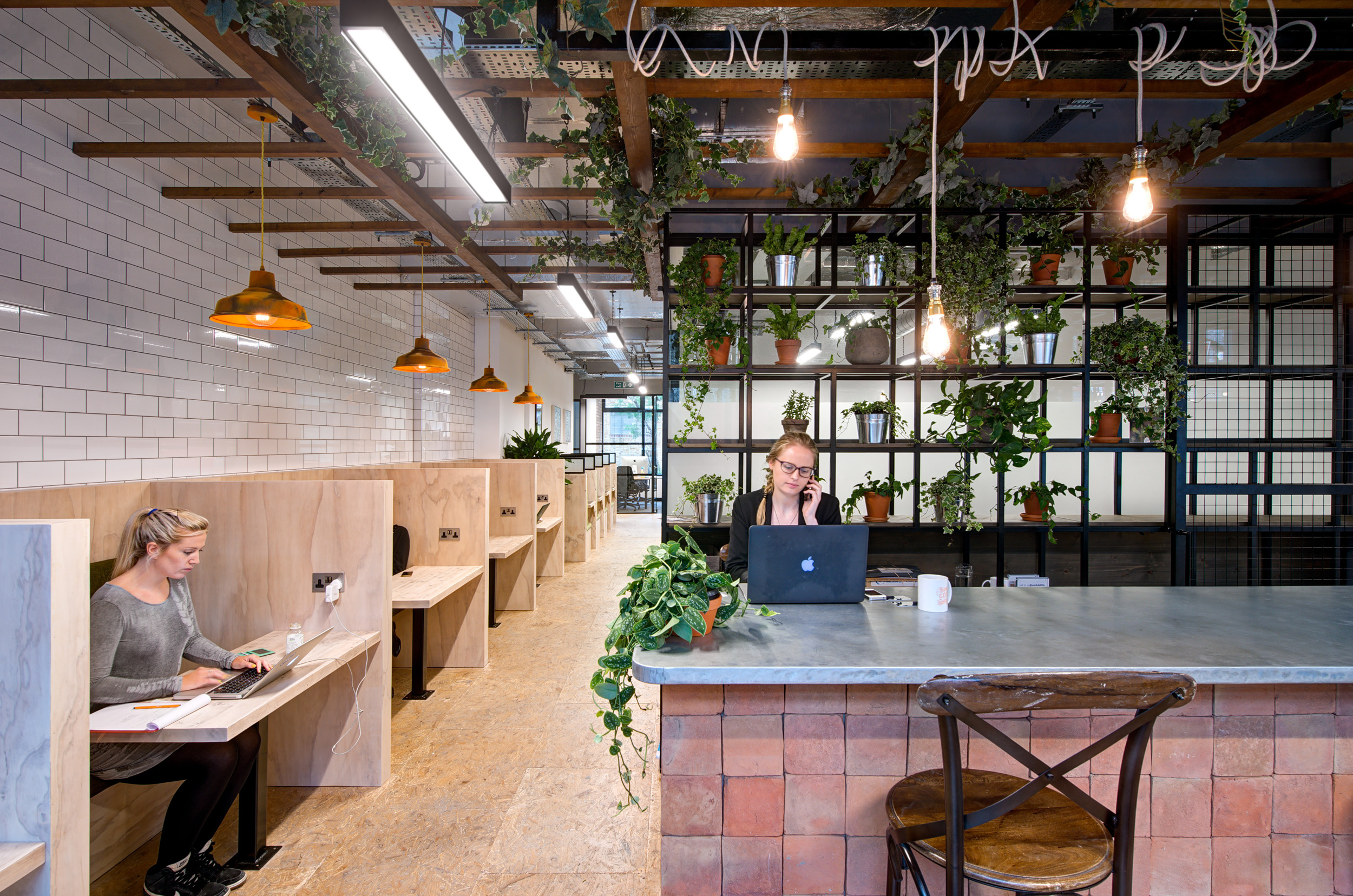 Worklife London Fields vibrant biophilic teapoint seating space at designed by Modus, featuring wooden workstations, green plants, and natural lighting to create an inspiring work environment.