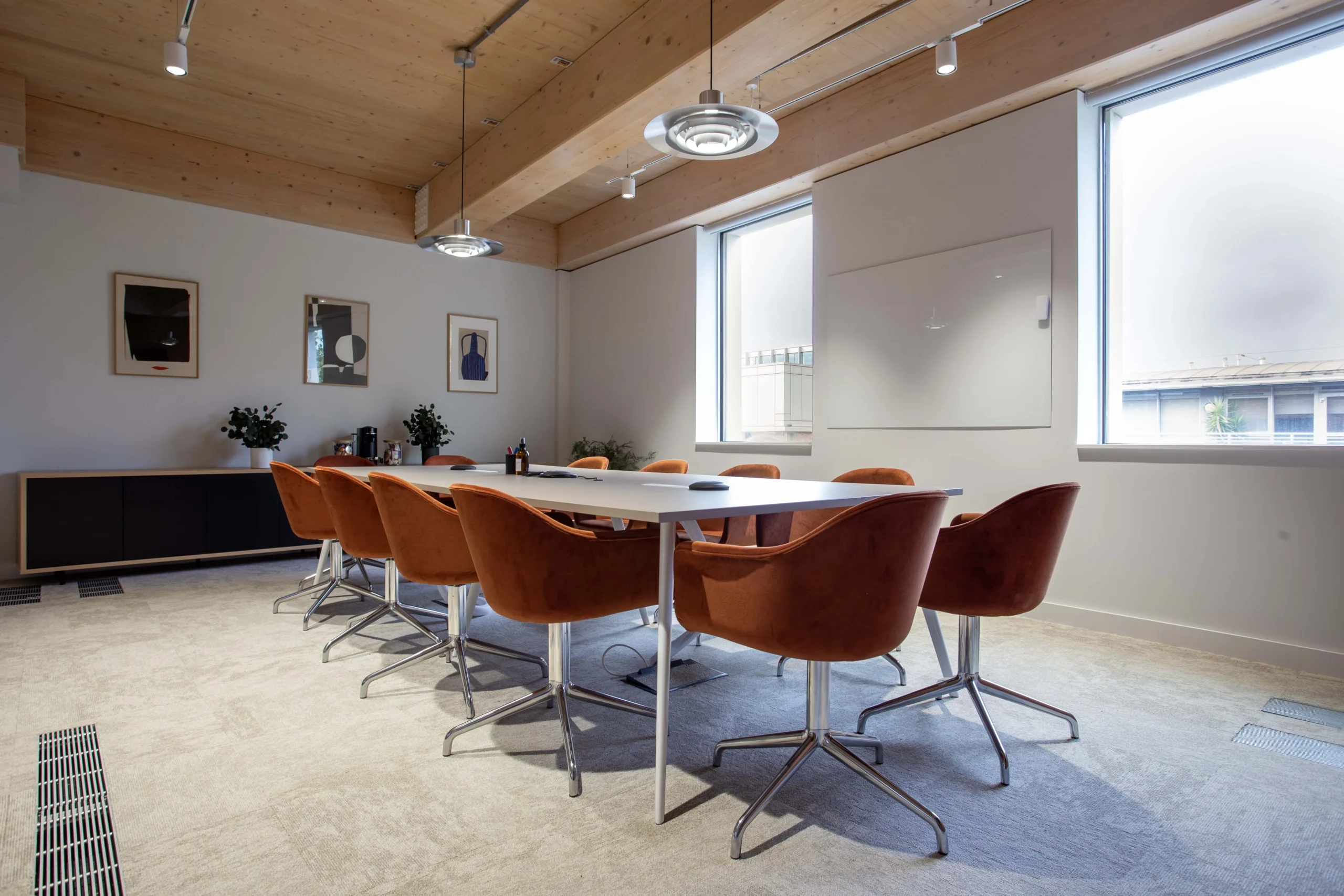 Techspace's meeting room with orange office chairs and a large table. Hanging lights and framed art decorates the space, creating a sleek and fresh environment.