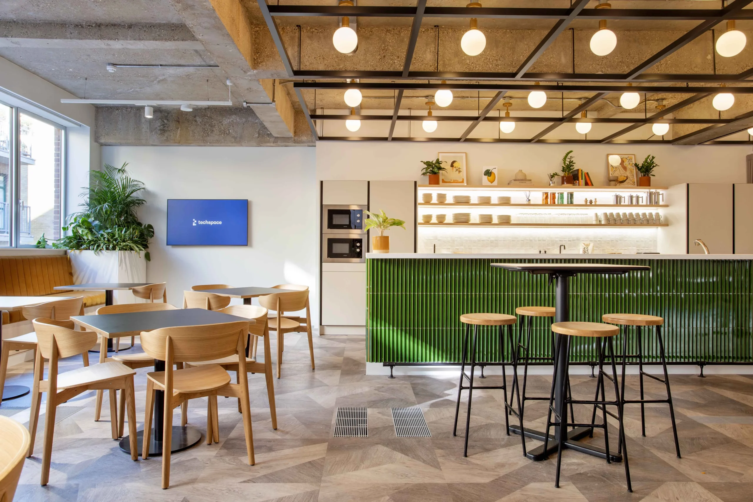 Techspace's teapoint and screen, featuring a TV screen with the brand logo in blue, bar stools and overhead lighting.