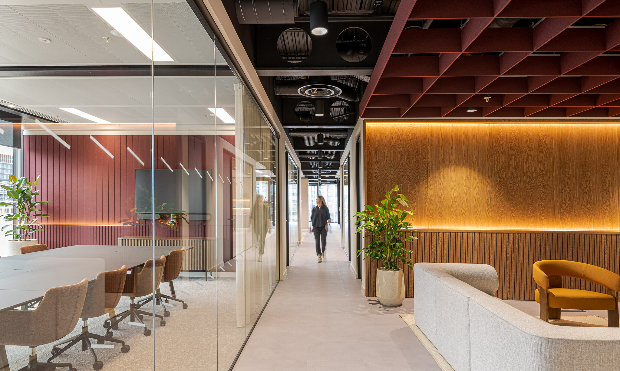 Corridor and meeting space at Arbor Level 4, part of the Tenant-Ready™ scheme by Modus, with exposed services overhead, glazed partitions, a timber-lined lounge wall and a boardroom featuring red acoustic panelling.
