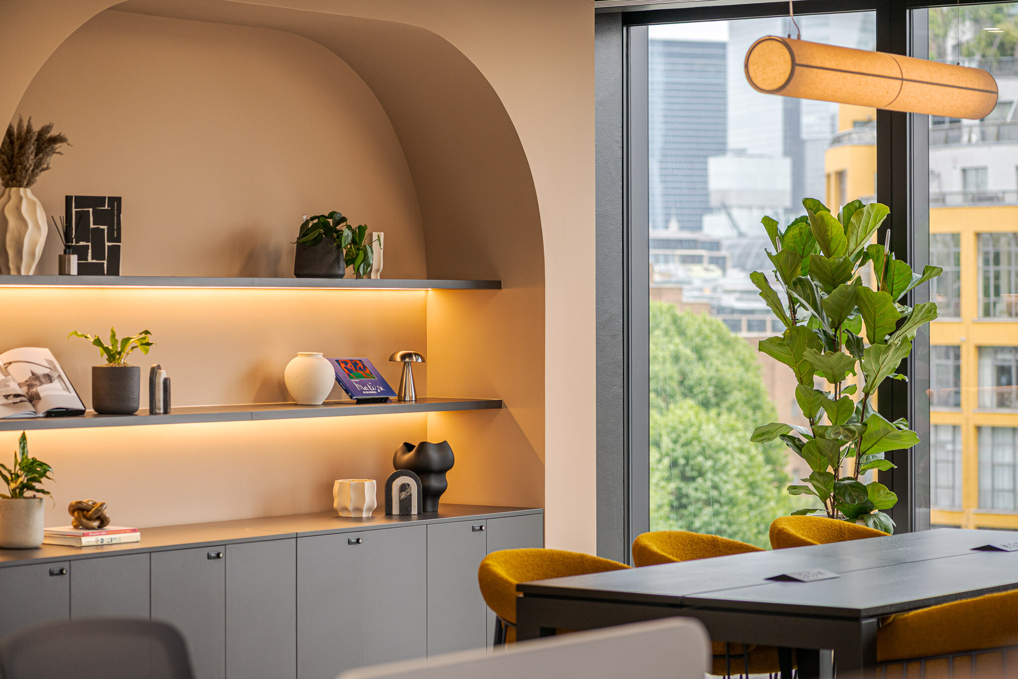 Close-up of the arched shelving nook in the Arbor Level 4 Tenant-Ready™ fit out by Modus, styled with curated décor, soft integrated lighting, and a backdrop of mustard chairs beside full-height glazing.
