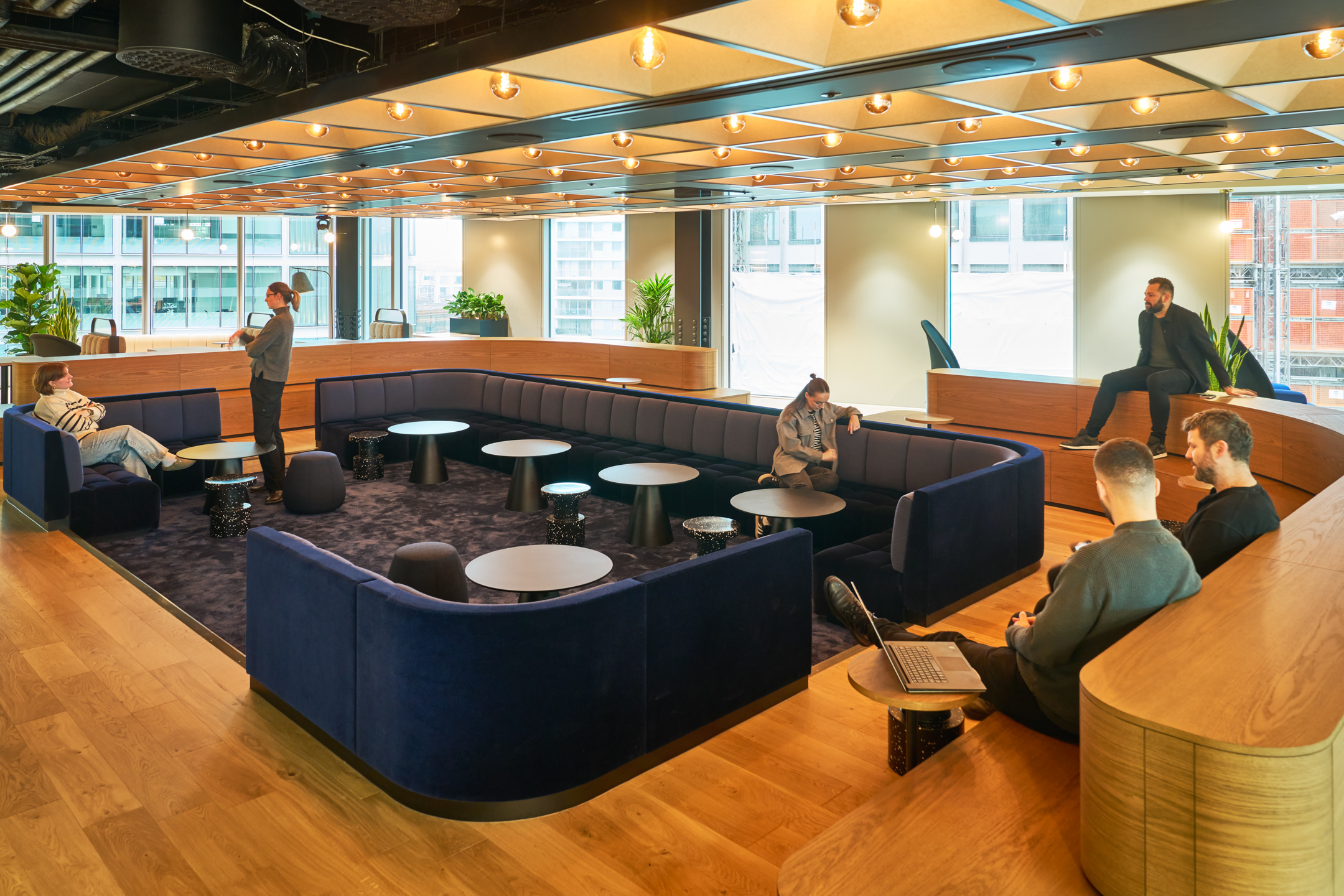 Clubhouse-style breakout space for International Technology and Data Firm, with sunken navy seating, round tables and timber tiered benches designed for informal meetings, team catch-ups and social connection.