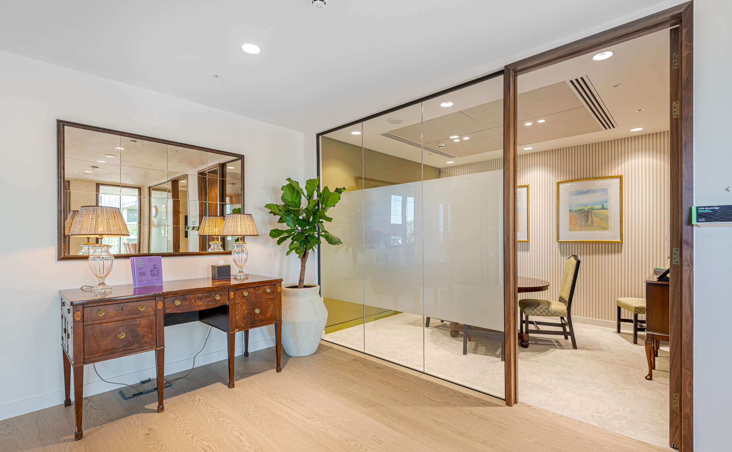 Executive meeting suite at an Investment Management Firm featuring glazed partitions with privacy film. Traditional furnishings and striped wallpaper bring a heritage tone to the space. The fit out by Modus includes a decorative mirror, antique-style console, and soft ambient lighting.