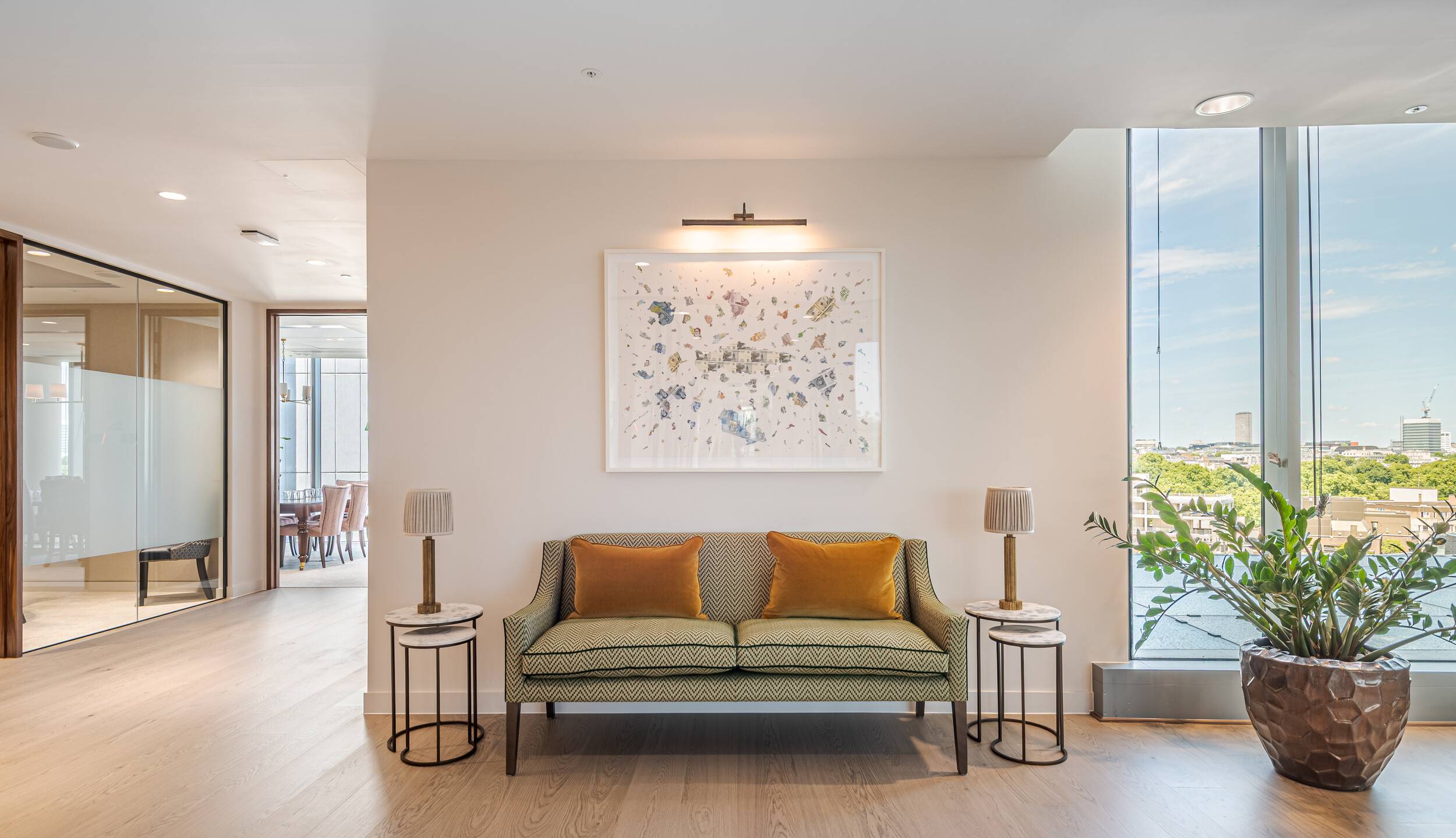 Window-side seating nook in an Investment Management Firm, styled with a patterned green sofa, ochre cushions, and marble side tables. Large glazing offers city views and floods the space with natural light. Part of a refined office fit out by Modus.