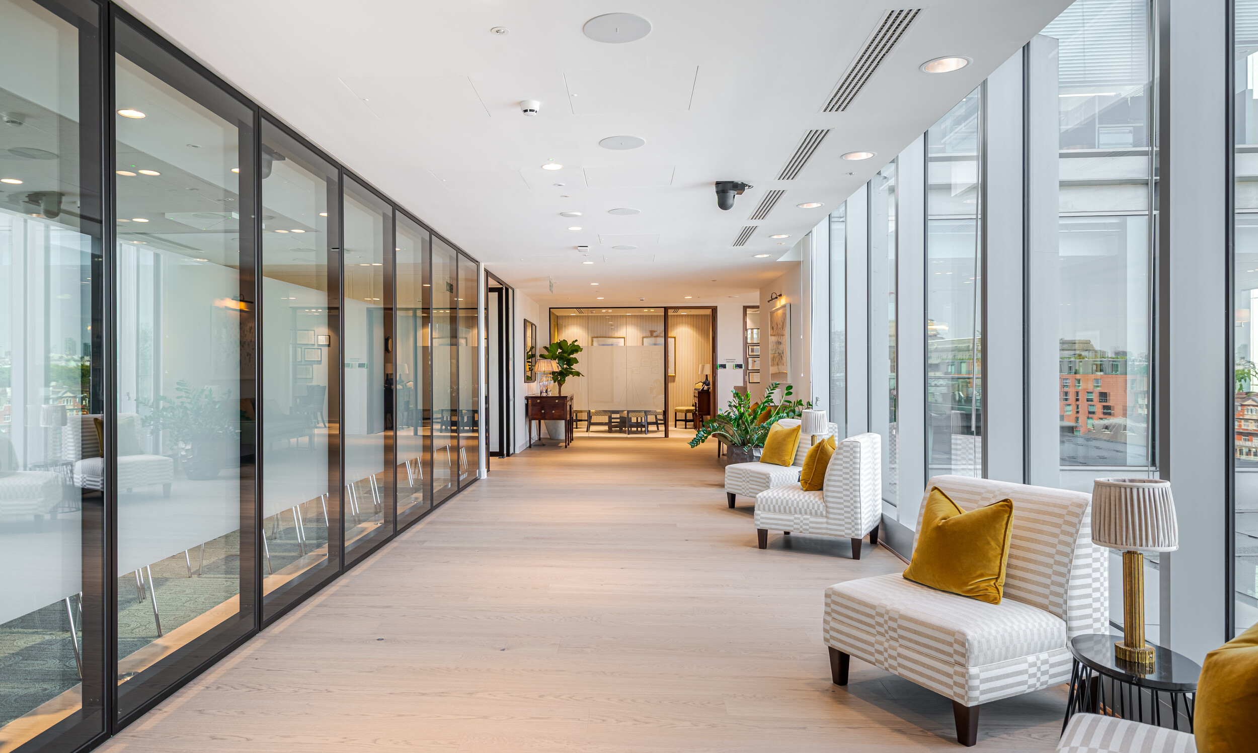 Glazed corridor in an Investment Management Firm lined with striped lounge chairs and ochre cushions. Floor-to-ceiling windows maximise daylight and city views. Modus designed the fit out to balance elegance with client-facing functionality.