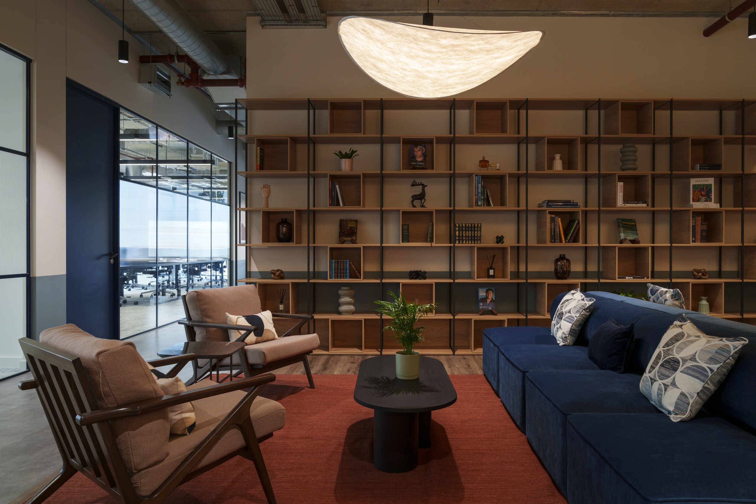 Breakout area at Newflex One Station Hill with a navy sofa, patterned cushions, wooden armchairs, and floor-to-ceiling shelving behind a black coffee table.