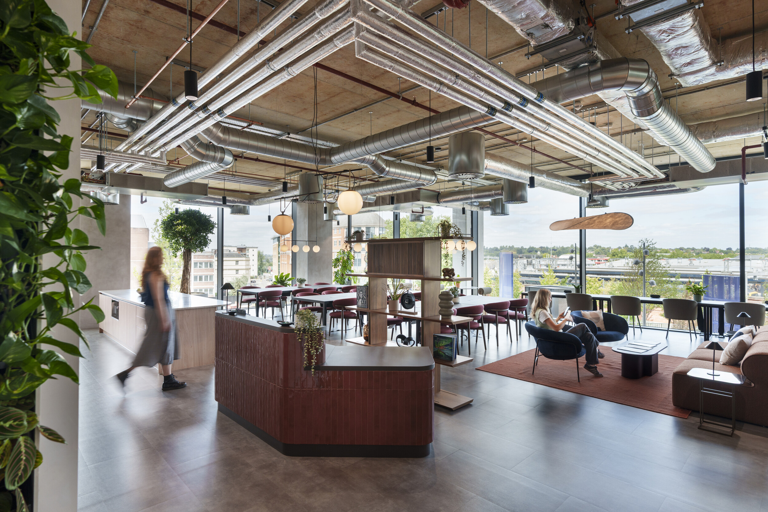 Breakout area at Newflex One Station Hill with floor-to-ceiling windows, exposed ceiling services, greenery, and a mix of seating areas.