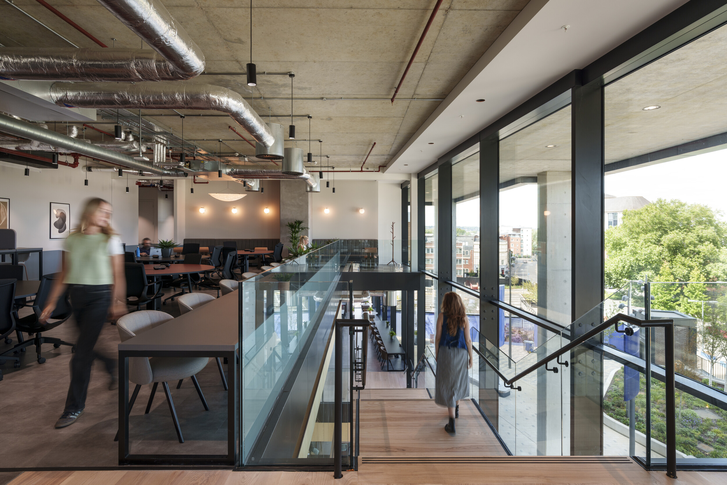 Workspace at Newflex One Station Hill with open desks, glass balustrades, exposed ceiling services, and full-height windows overlooking the city.