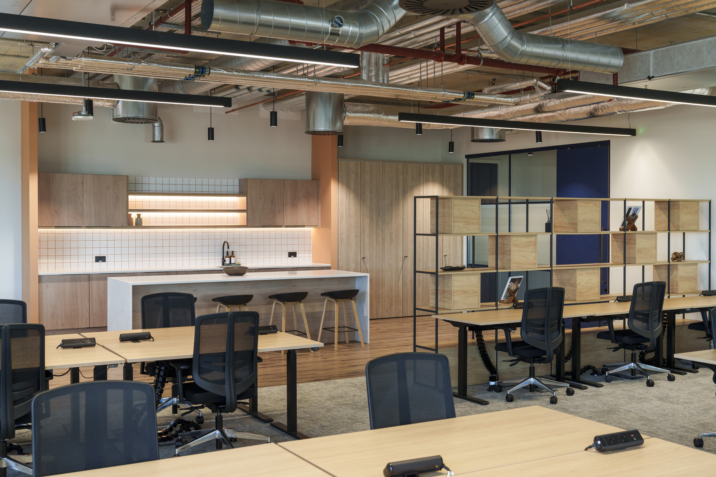 Open-plan office at Newflex One Station Hill with shared desks, black task chairs, a tiled kitchenette, and wooden shelving partitions.