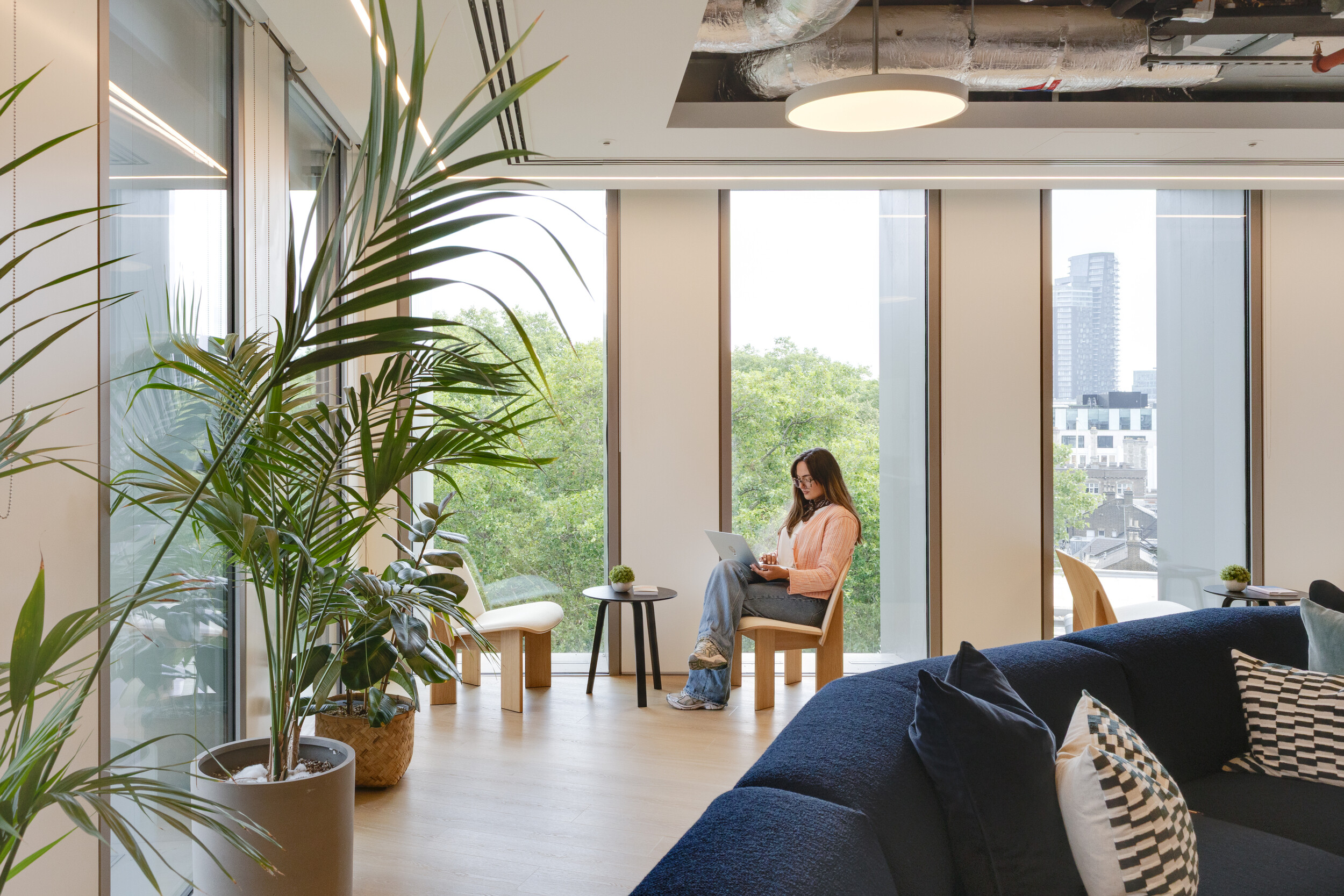 Capital on Tap office lounge with large windows, indoor plants, and a professional working on a laptop in a bright, modern setting.