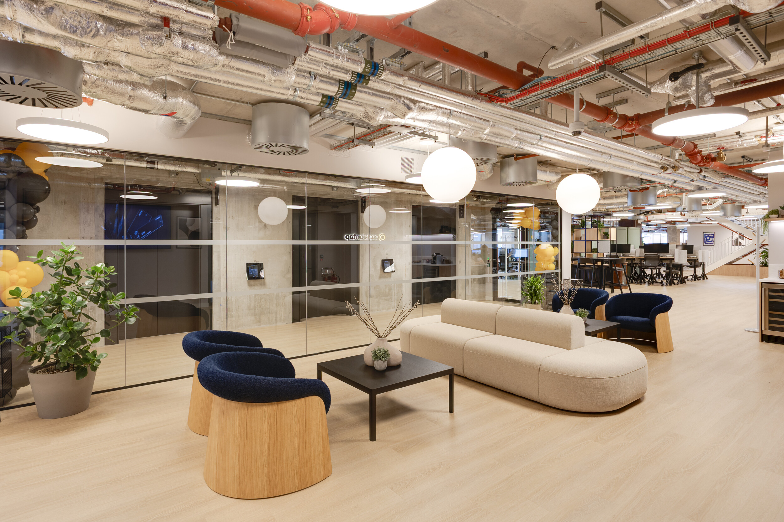 Capital on Tap lounge area with cream sofa, blue armchairs, indoor plants, and glass-partitioned offices within an open-plan workspace.