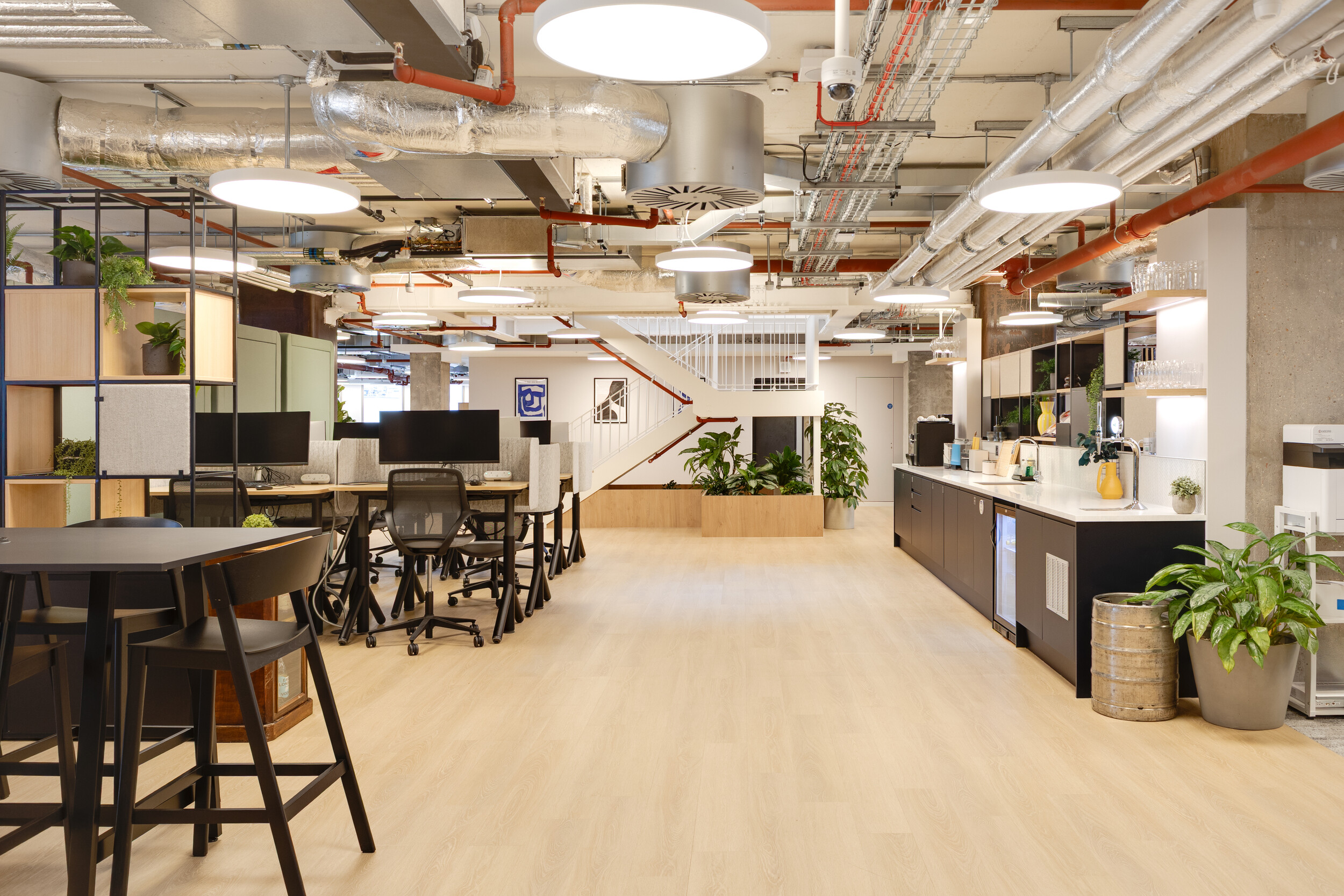 Capital on Tap open-plan workspace with shared desks, exposed ceilings, indoor plants, and a long teapoint with modern finishes.