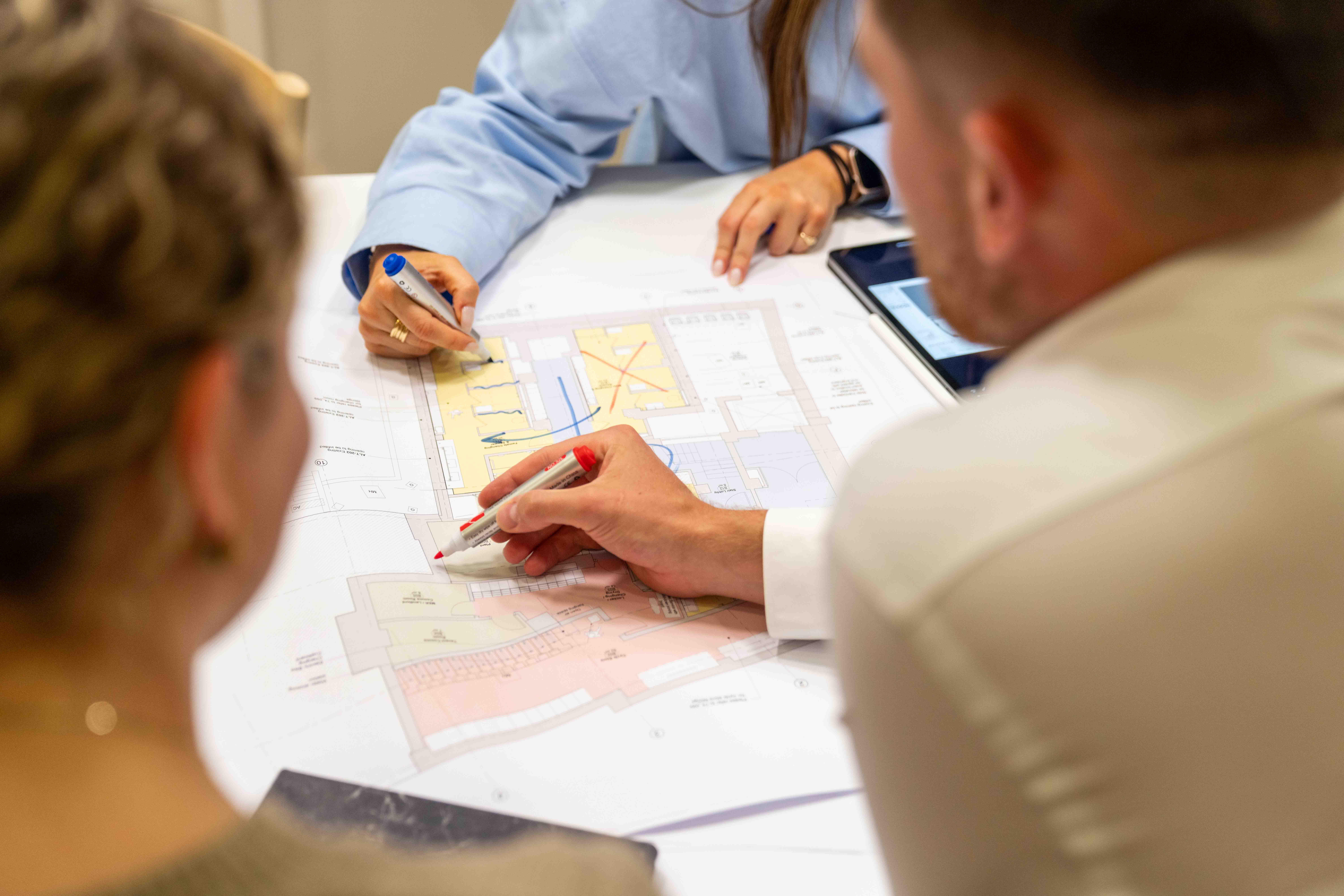 Group collaborating over detailed floor plans, using coloured markers to review and discuss layout designs during a planning session.
