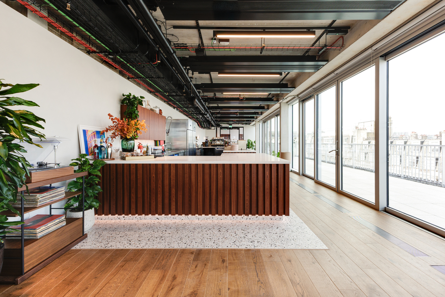 The Space House Clubhouse bar area featuring a walnut-fluted counter, terrazzo flooring, and expansive glazing, part of Modus’ transformation of the iconic London landmark.