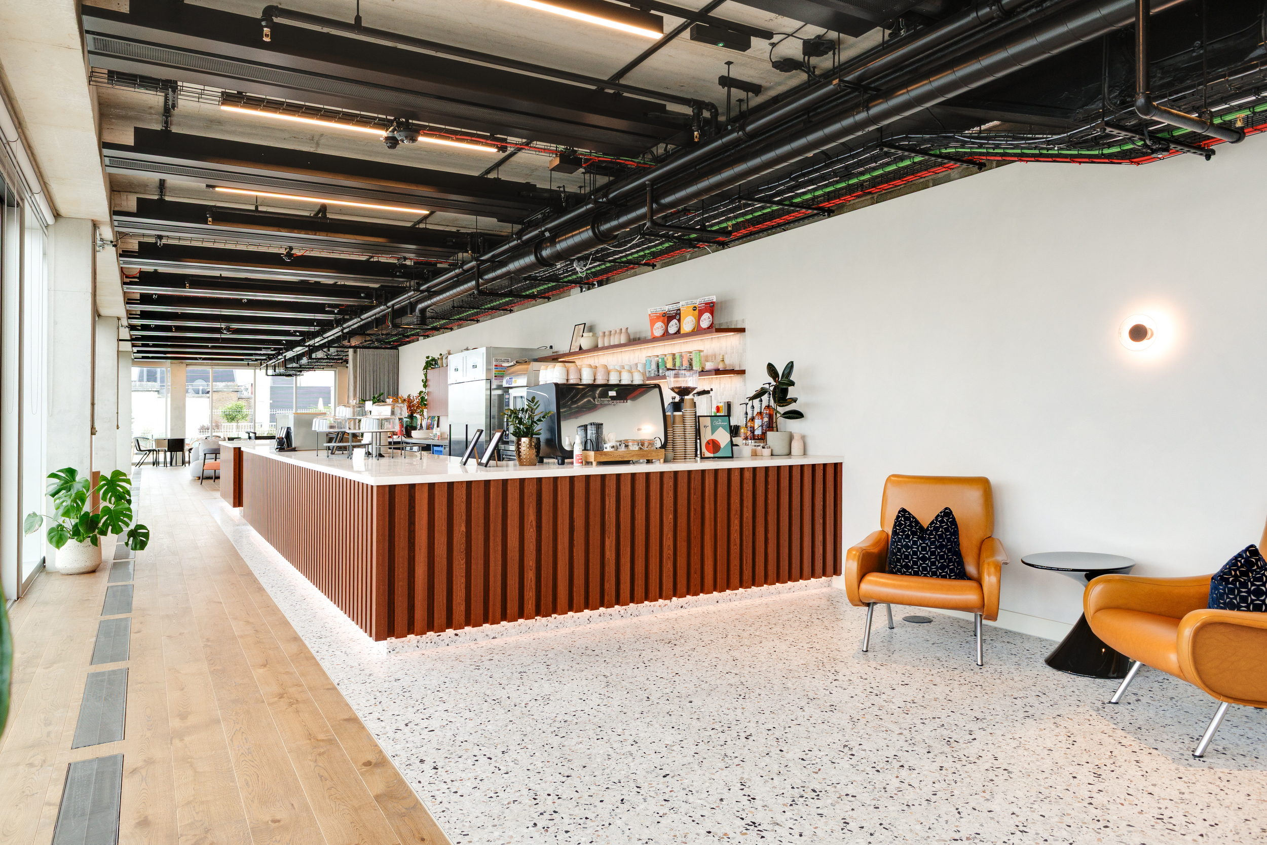 Interior view of the Space House Clubhouse café area designed by Modus, showing a walnut-fluted counter, terrazzo flooring, and leather seating with expansive city views.