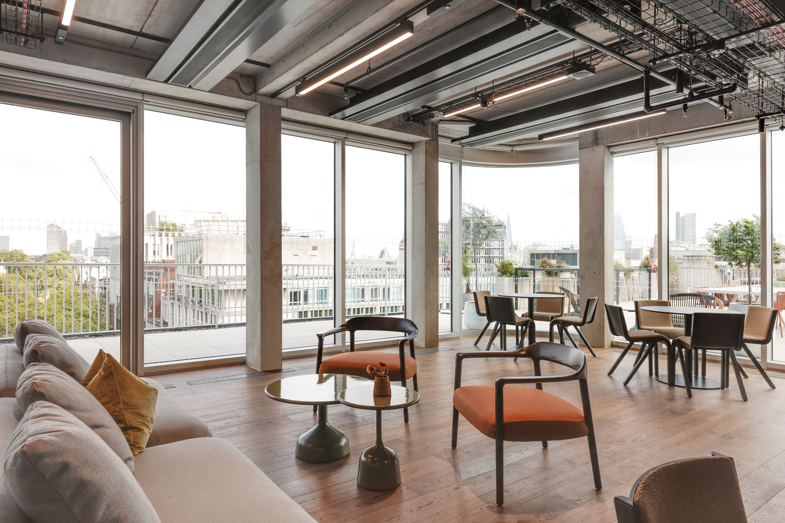 Lounge area within the Space House Clubhouse designed by Modus, featuring timber flooring, soft seating in warm tones, and panoramic glazing overlooking London.