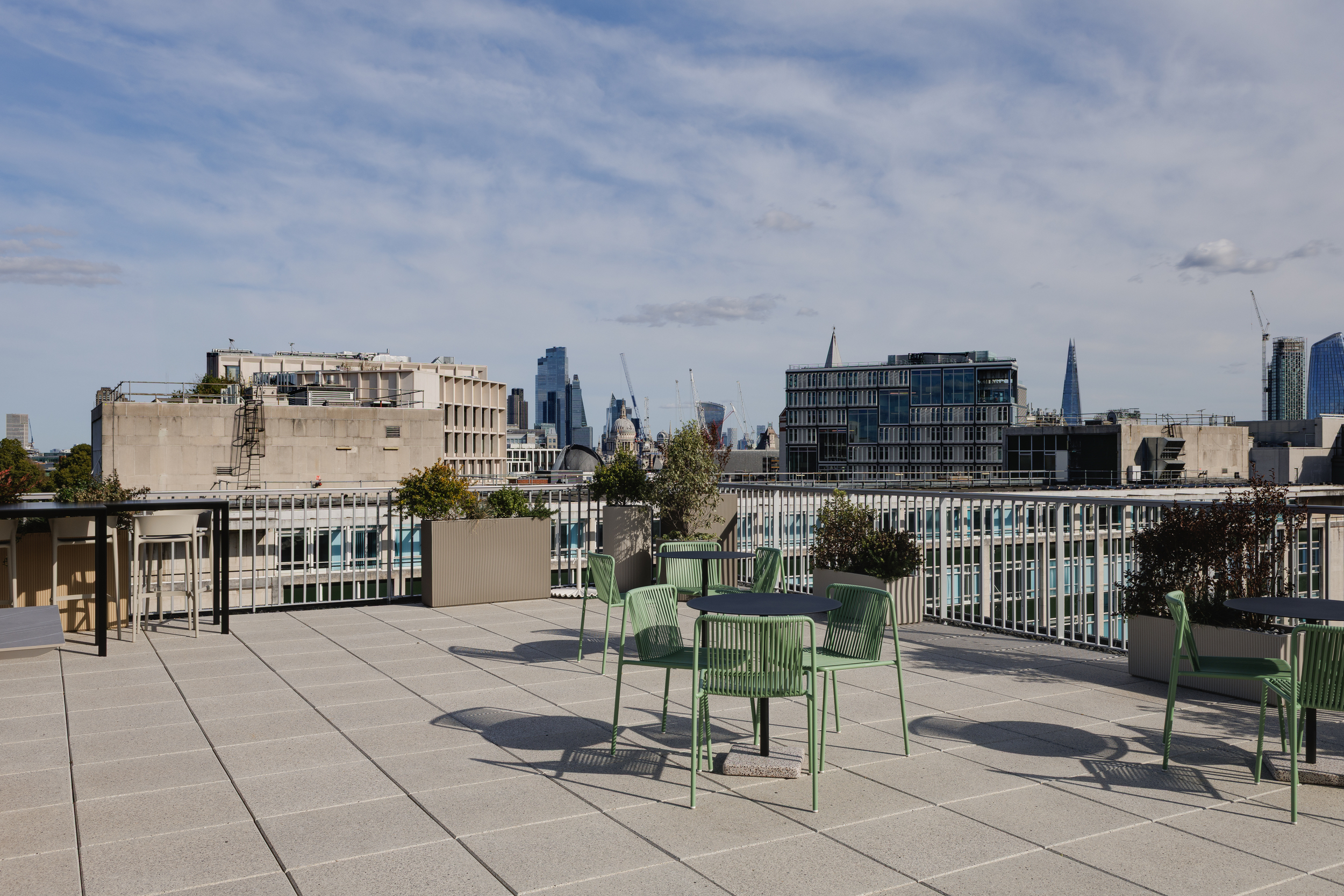 Open-air terrace at the Space House Clubhouse designed by Modus, with green seating, planters, and panoramic views towards London landmarks including The Shard.