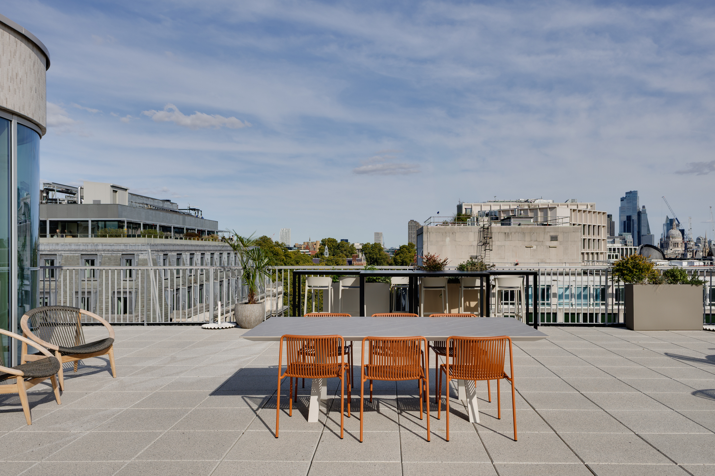 Outdoor terrace at the Space House Clubhouse by Modus, with orange dining chairs, planters, and views across London’s skyline.