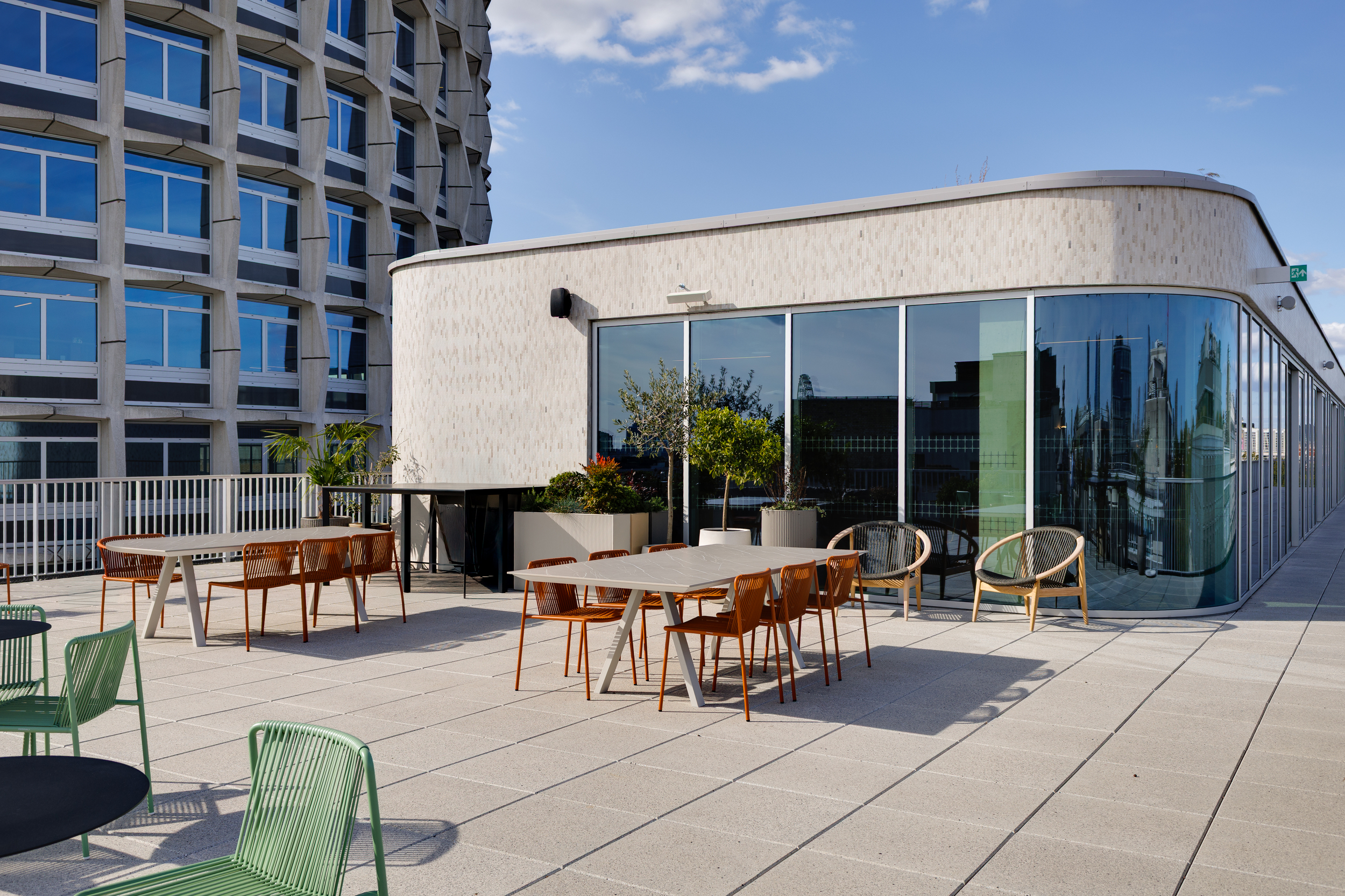 The Space House Clubhouse terrace with green and orange seating, curved glazing, and views of the building’s Brutalist façade, designed as a social space by Modus.